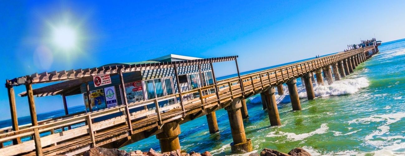 A wooden pier extending into the Atlantic on the Namibian coast, sun rising over the water.